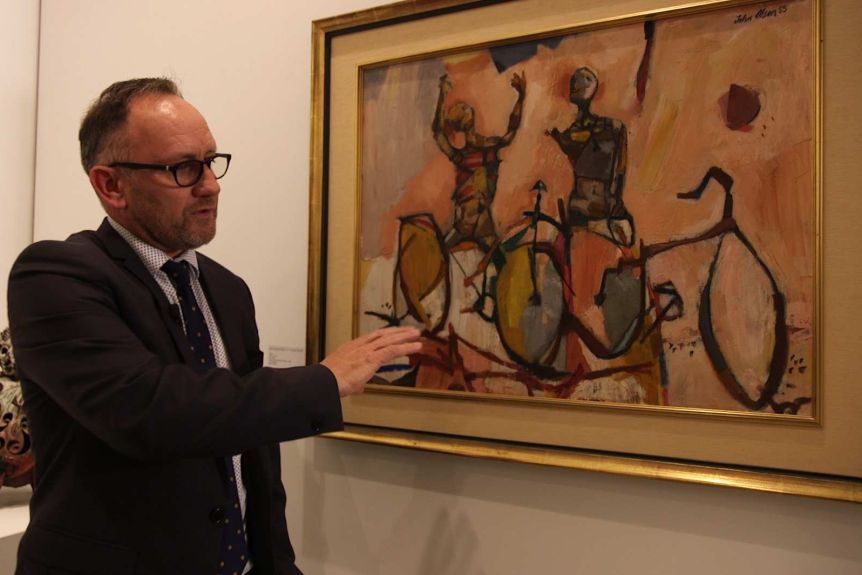 Deutscher and Hackett's Henry Mullholland with John Olsen's work The Bicycle Boys Rejoice, one of the most well known paintings in the James Fairfax collection. (ABC News)